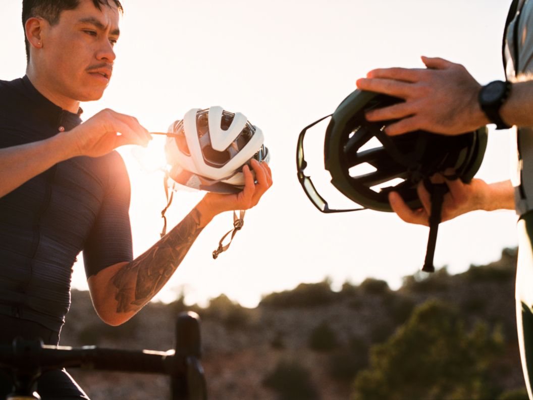 Two riders stand while holding their helmets and sunglasses during golden hour.t. 